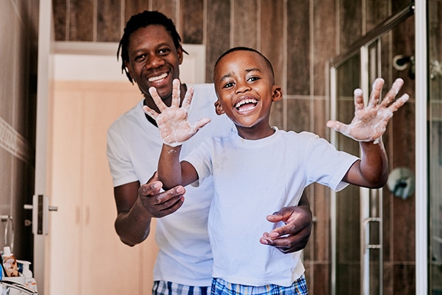 Father & son playfully washing their hands together in the bathroom smiling